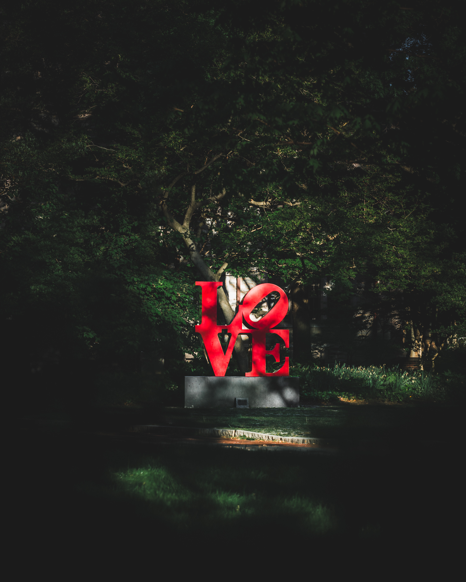Red LOVE statue on University of Pennsylvania campus nestled within green forestation