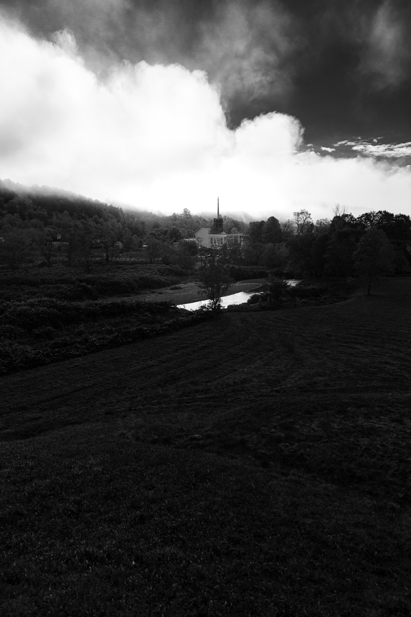 A black and white photo of the Stowe Community Church in front of ominous clouds