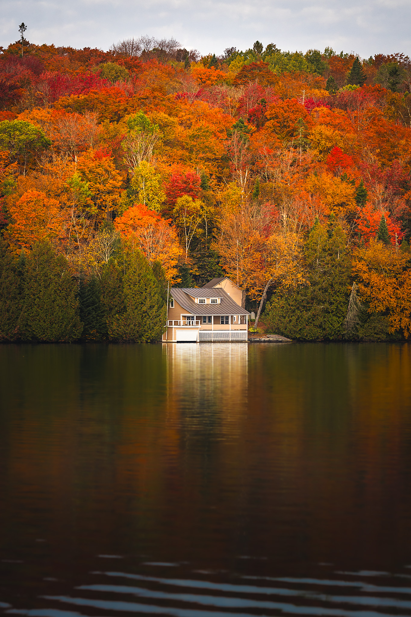 A lone house on the water of Joe’s Pond nestled within brilliant red, orange, yellow, and green fall foliage