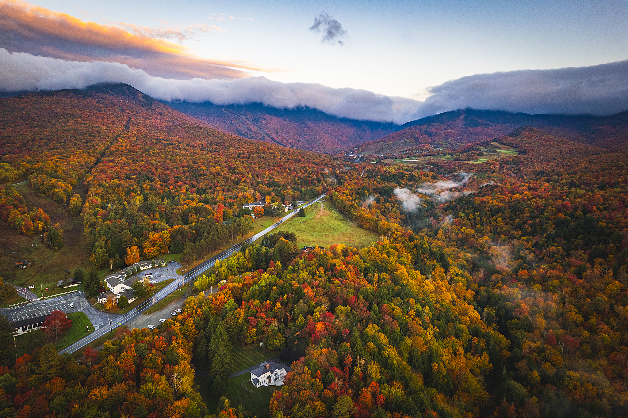 Overhead shot of beautiful Stowe, Vermont orange, yellow, red, and green fall foliage at sunrise with fog rolling over the hills