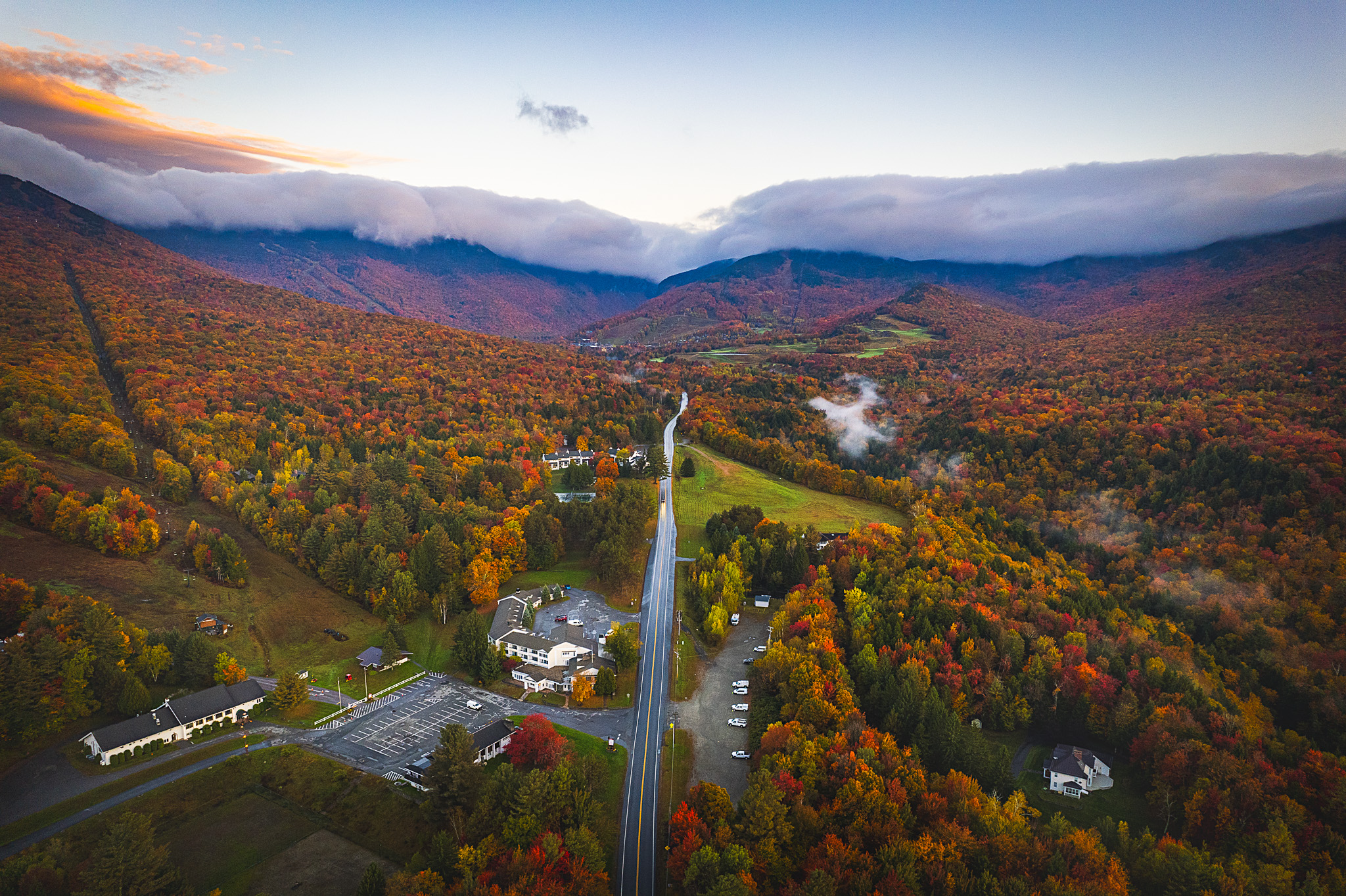 Overhead shot of beautiful Stowe, Vermont orange, yellow, red, and green fall foliage at sunrise with fog rolling over the hills