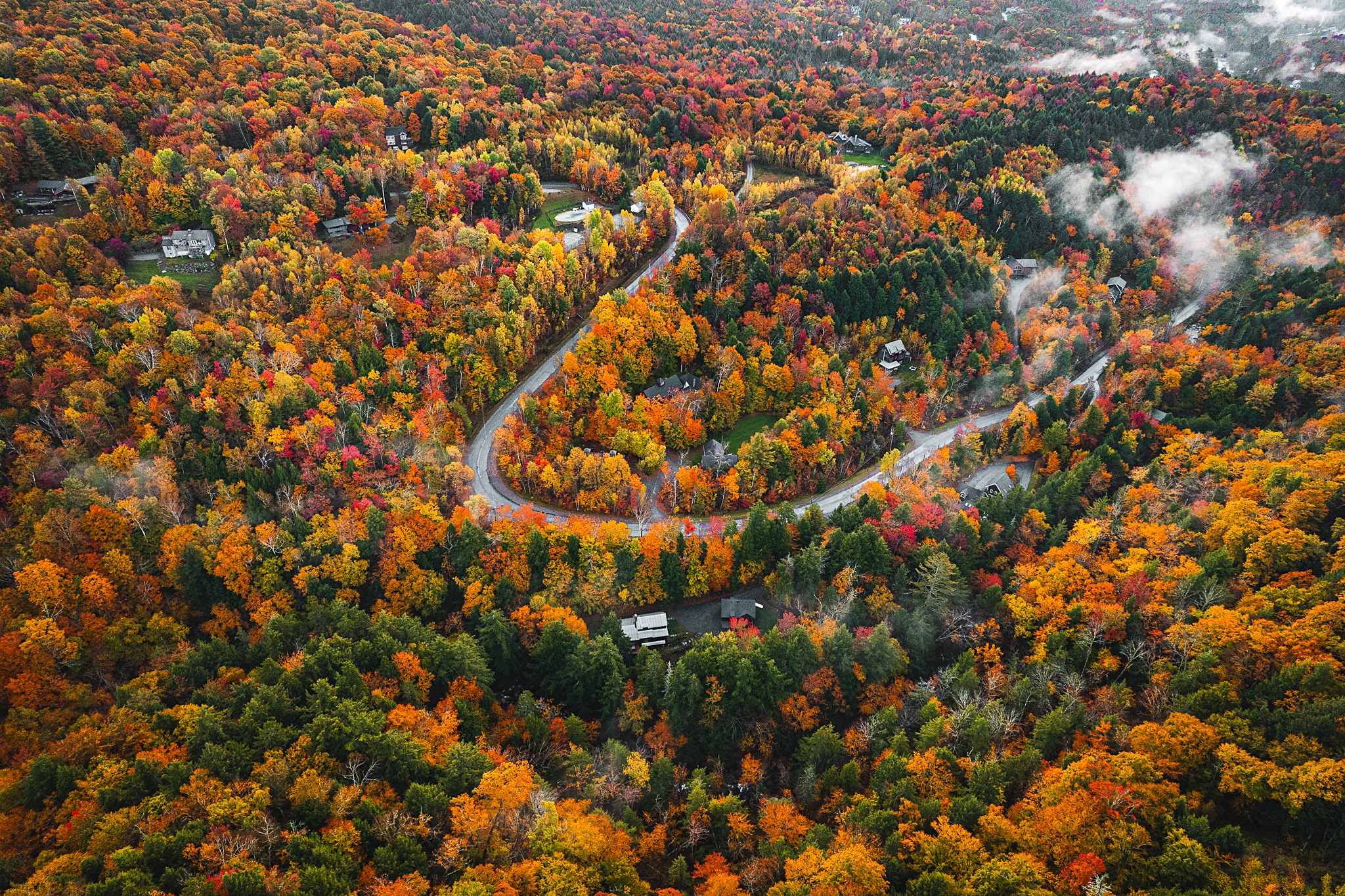 Overhead shot of a U-shaped switchback in Stowe, Vermont orange, yellow, red, and green fall foliage with clouds in the foreground