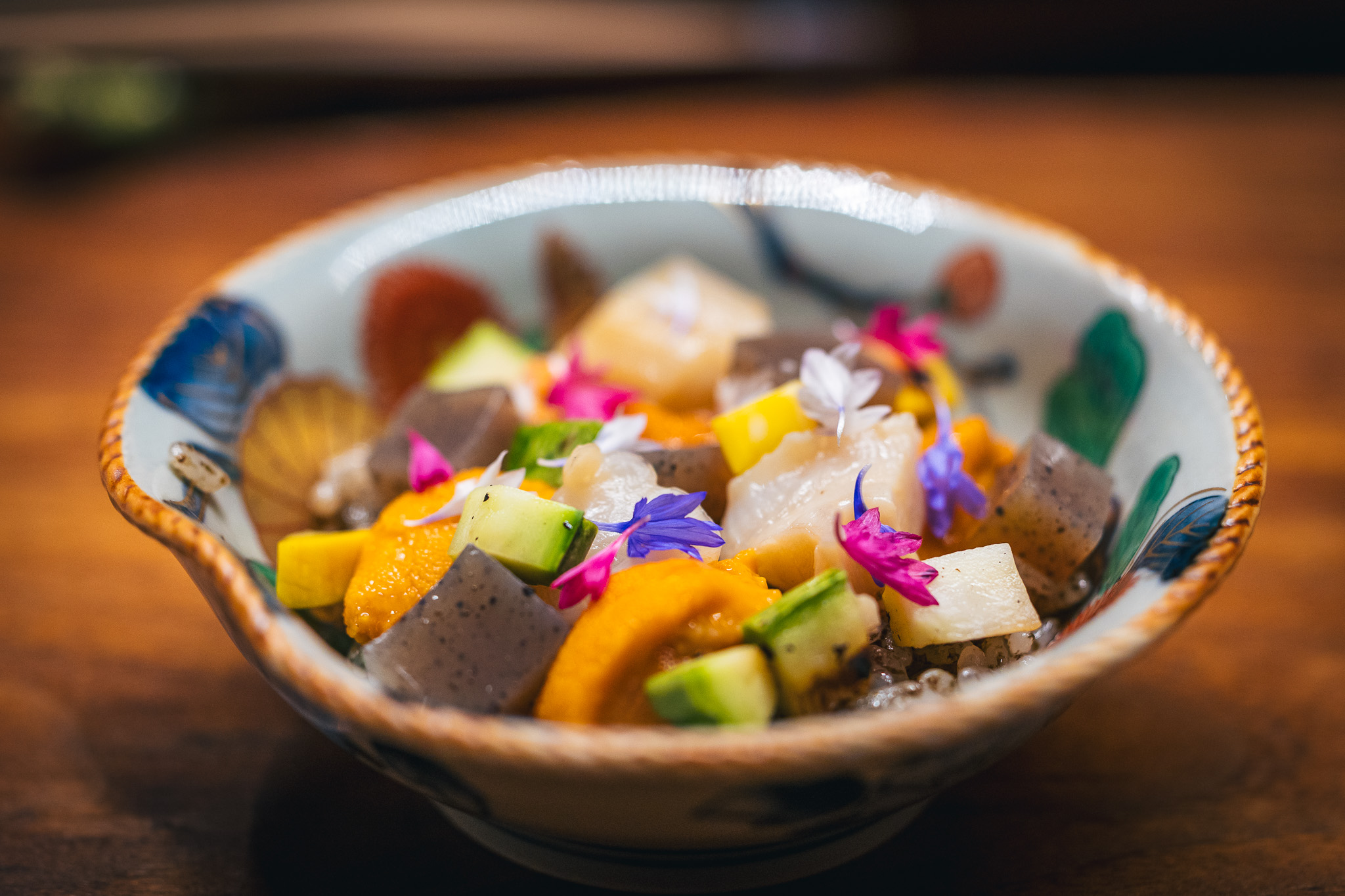 Small bowl with sushi, edible flowers, vegetable, and fish