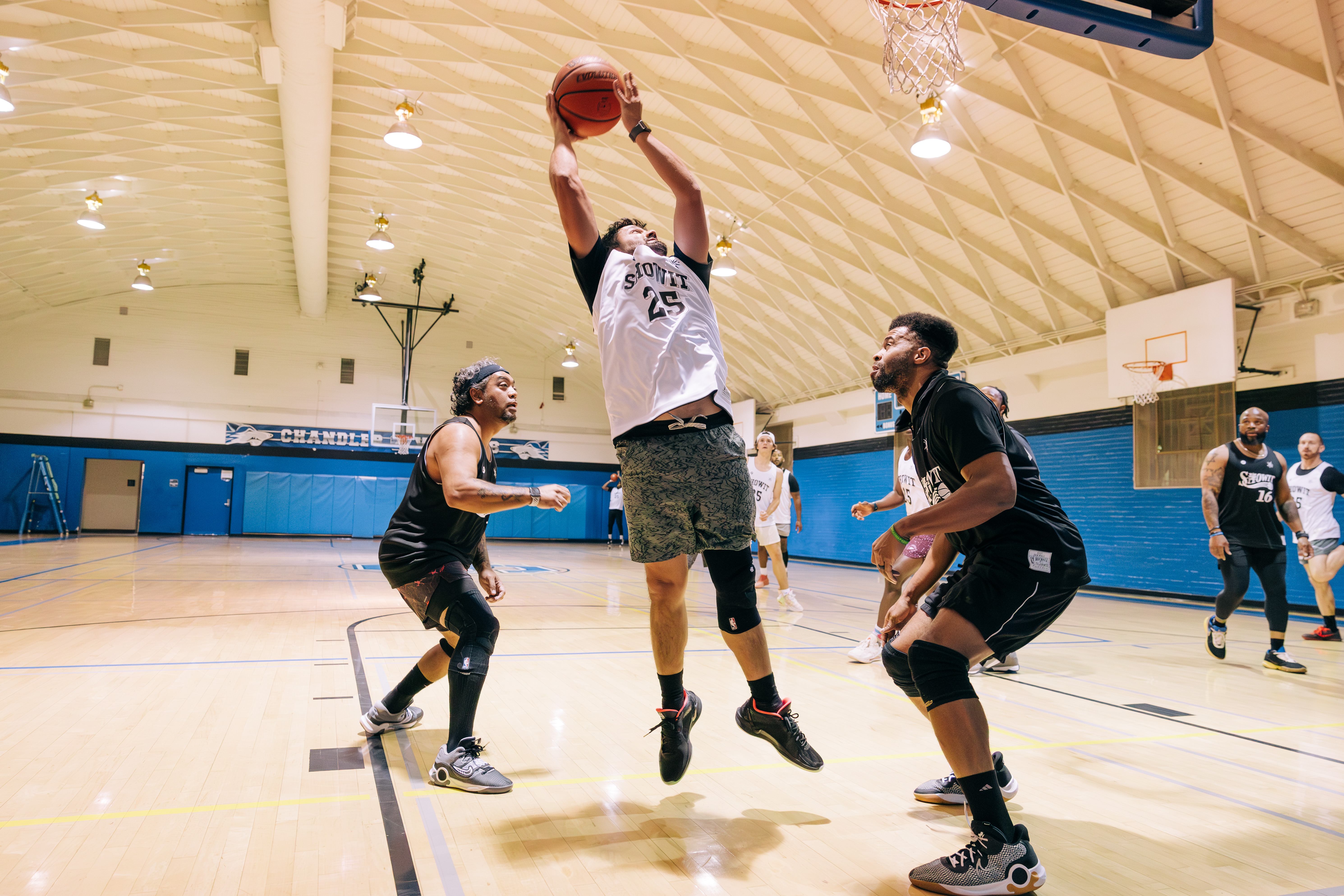 Man shooting a basketball over two defenders