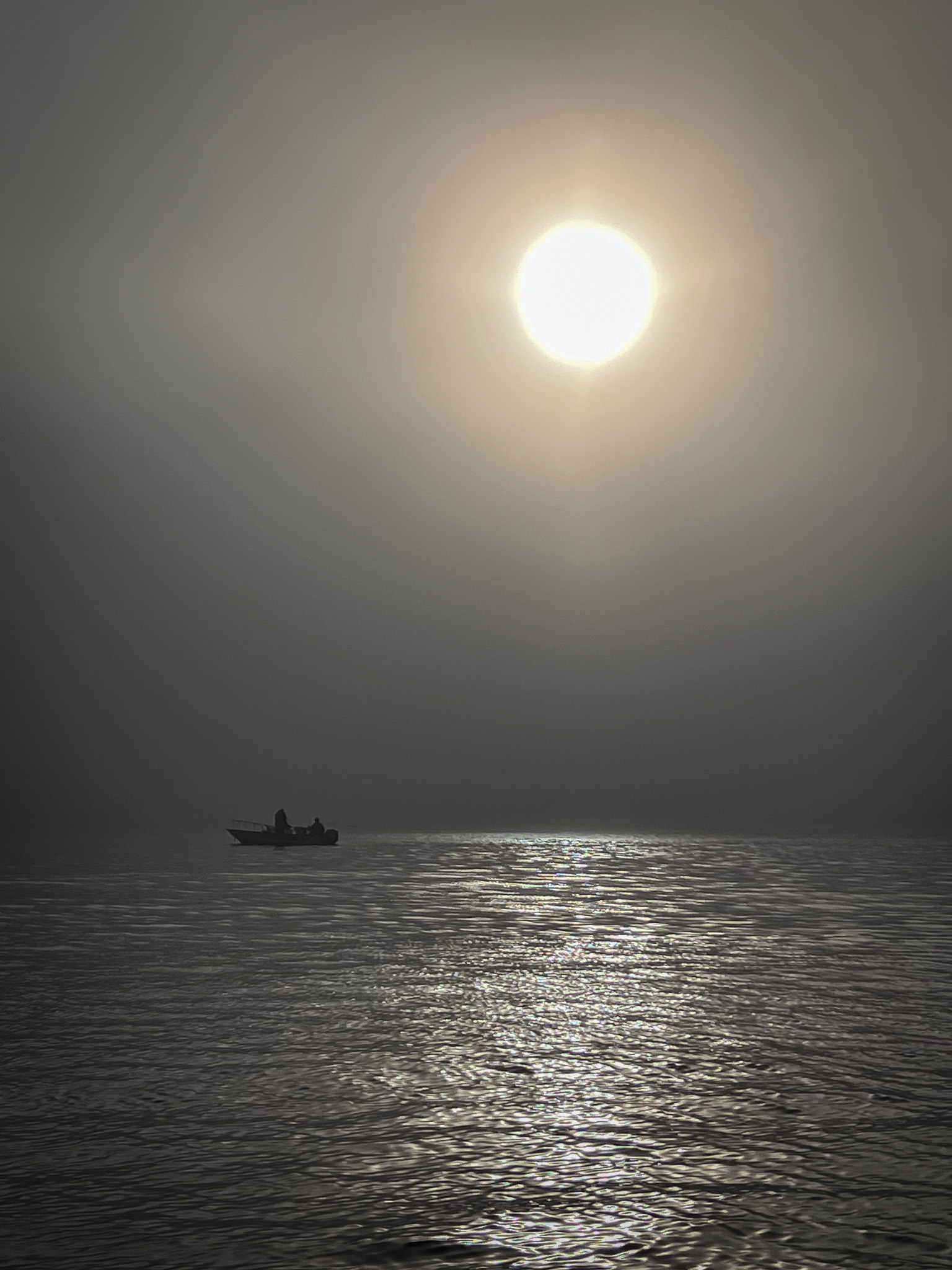 A lone boat on the water during a foggy sunrise